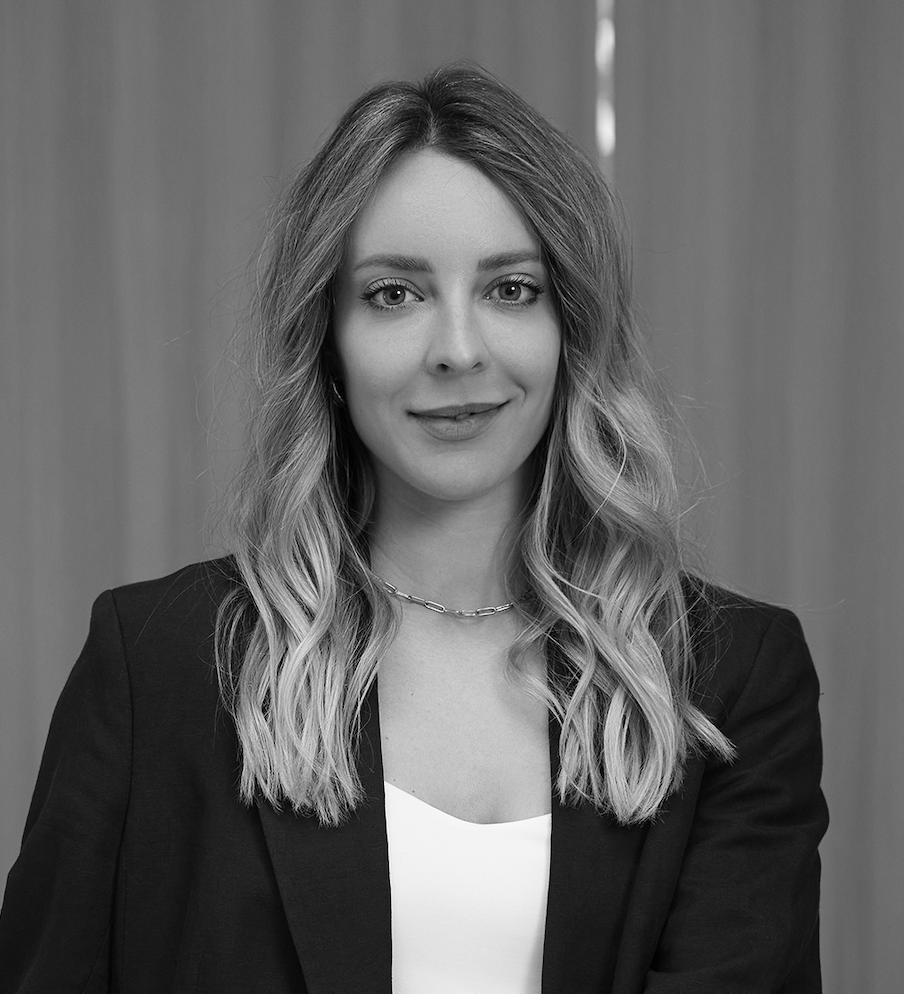 Nadine Loepfe, smiling, in a dark blazer, photographed against a grey curtain.